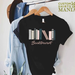 May include: Black t-shirt with a graphic of a stack of colorful books and the text "Booktrovert".