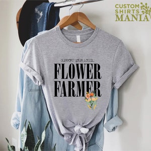 May include: A gray t-shirt with the text "Support Your Local Flower Farmer" in black lettering. A small bouquet of flowers is printed below the text.