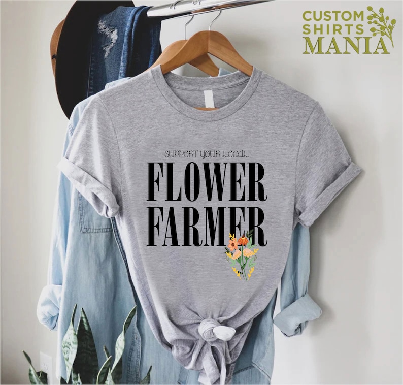 May include: A gray t-shirt with the text "Support Your Local Flower Farmer" in black lettering. A small bouquet of flowers is printed below the text.