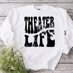 May include: White sweatshirt with black text that reads "Theater Life" in a retro, distressed font.