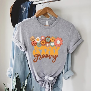 May include: A gray t-shirt with a retro-style graphic design featuring a bouquet of flowers and the text "Stay Groovy".