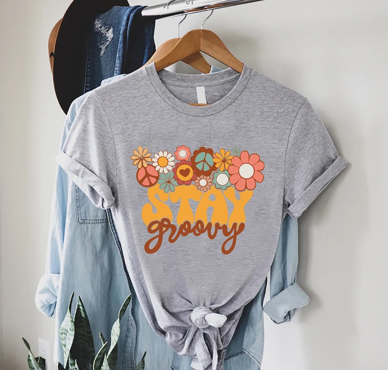 May include: A gray t-shirt with a retro-style graphic design featuring a bouquet of flowers and the text "Stay Groovy".