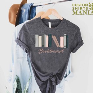 May include: A dark gray t-shirt with a graphic of a stack of colorful books and the text "Booktrovert".
