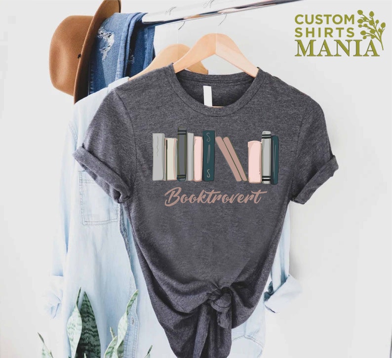 May include: A dark gray t-shirt with a graphic of a stack of colorful books and the text "Booktrovert".