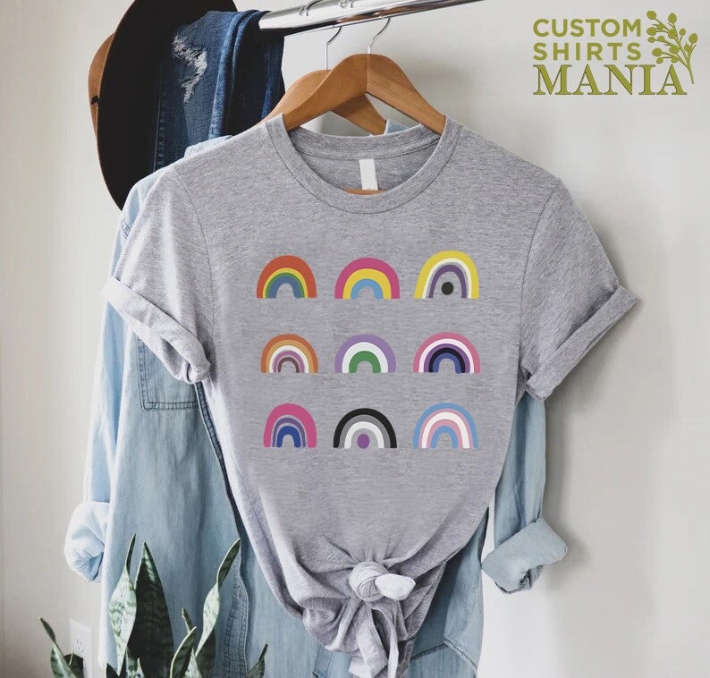 K&ouml;nnte beinhalten: Ein graues T-Shirt mit einem Design aus neun verschiedenen bunten Regenb&ouml;gen. Die Regenb&ouml;gen sind in drei Reihen zu je drei angeordnet. Der Text "CUSTOM SHIRTS MANIA" befindet sich in der oberen rechten Ecke des Bildes.