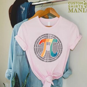 Może przedstawiać: R&oacute;żowy T-shirt z tęczowym symbolem pi. Symbol pi składa się z pierwszych 100 cyfr pi. Tekst "Pi = 3,14..." jest napisany wewnątrz symbolu pi.