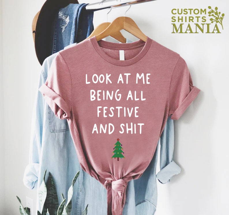 May include: A pink t-shirt with the text "Look at me being all festive and shit" in white lettering and a small green Christmas tree with lights below the text.