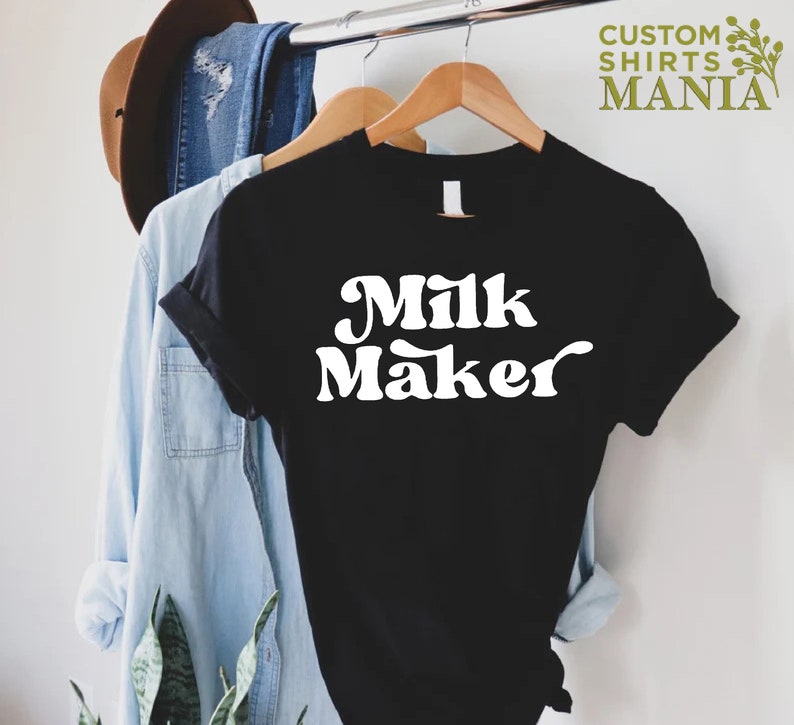 May include: Black t-shirt with white text that reads "Milk Maker" in a retro font.