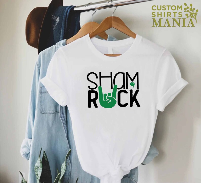 Peut inclure: T-shirt blanc avec du texte noir qui dit "Shamrock" avec un tr&egrave;fle vert et une main verte faisant le signe rock and roll.