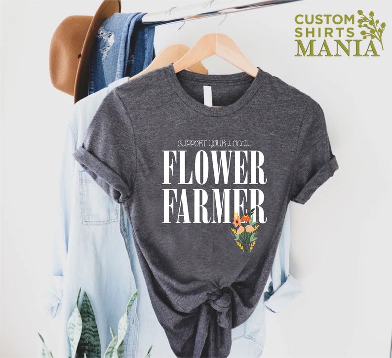 May include: A dark gray t-shirt with the text "Support your local Flower Farmer" in white. The shirt has a floral design in orange, yellow, and green.