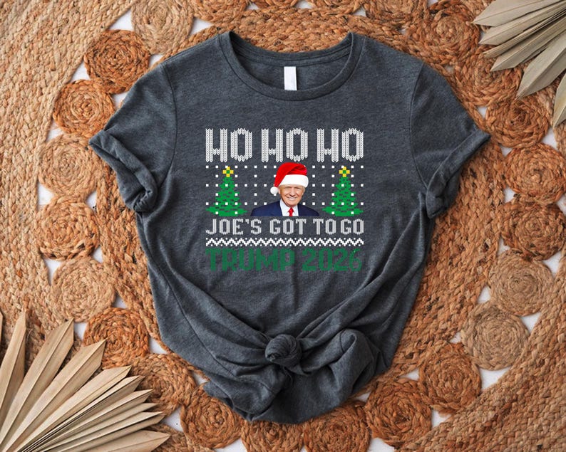 Op de afbeelding: Een donkergrijs gem&ecirc;leerd T-shirt met korte mouwen, voorzien van een wit breipatroon, de tekst HO HO HO, een afbeelding van Donald Trump met een kerstmuts tussen twee groene kerstbomen, de tekst JOE'S GOT TO GO en TRUMP 2024.