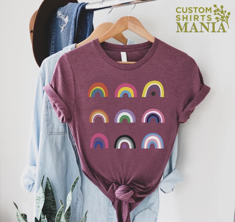 K&ouml;nnte beinhalten: Ein maronfarbenes T-Shirt mit einem Design aus neun verschiedenen bunten Regenb&ouml;gen. Die Regenb&ouml;gen sind in drei Reihen zu je drei angeordnet. Der Text "CUSTOM SHIRTS MANIA" befindet sich in der oberen rechten Ecke des Bildes.