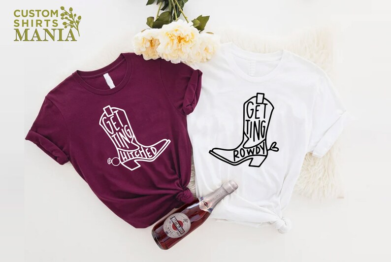 May include: Two t-shirts with a boot design and text. The maroon shirt says "Getting Hitched" and the white shirt says "Getting Rowdy".