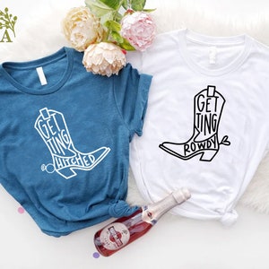 May include: Two t-shirts with a white cowboy boot graphic. The text on the blue shirt says "Getting Hitched" and the text on the white shirt says "Getting Rowdy".