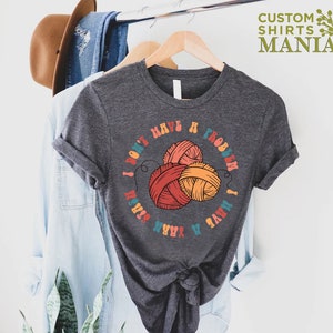 May include: A dark gray t-shirt with a colorful graphic that says "I don't have a problem I have yarn" with a circle of yarn balls in the center.