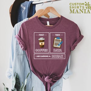 May include: A maroon t-shirt with a graphic design that says "First Coffee, Then Data, I am earning a Break". The graphic features a cup of coffee and a clipboard with a pen.