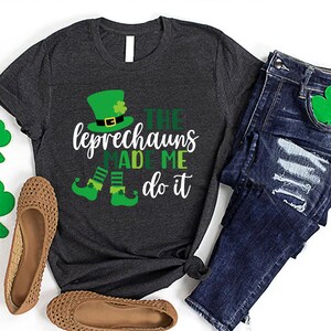 May include: A dark grey t-shirt with a white graphic of a leprechaun with the text "The Leprechauns Made Me Do It".