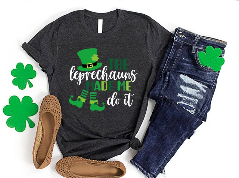 May include: A dark grey t-shirt with a white graphic of a leprechaun with the text "The Leprechauns Made Me Do It".