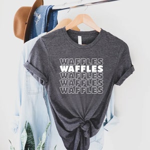 Może przedstawiać: Szary t-shirt z napisem "Waffles" powt&oacute;rzonym pięć razy na biało, ułożonym pionowo. Tekst jest w retro, pogrubionej czcionce.