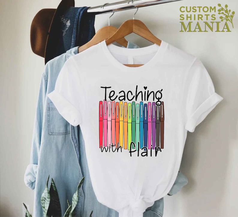 May include: White t-shirt with the text "Teaching with flair" and a graphic of colorful markers.