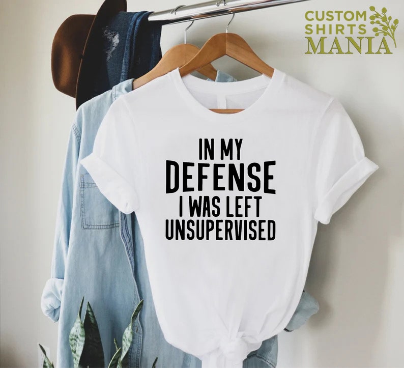 May include: White t-shirt with black text that reads "In my defense I was left unsupervised".