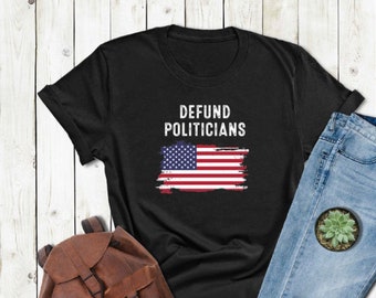 Puede incluir: Camiseta negra con el texto "DEFUND POLITICIANS" y un gráfico de bandera estadounidense desgastado.