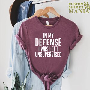 May include: A maroon t-shirt with white text that reads "In my defense I was left unsupervised".