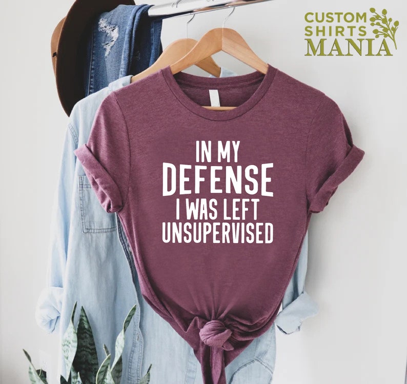 May include: A maroon t-shirt with white text that reads "In my defense I was left unsupervised".