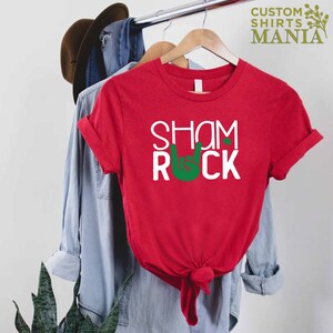 Peut inclure: T-shirt rouge avec du texte blanc qui dit "Shamrock" et un symbole de main rock and roll vert.
