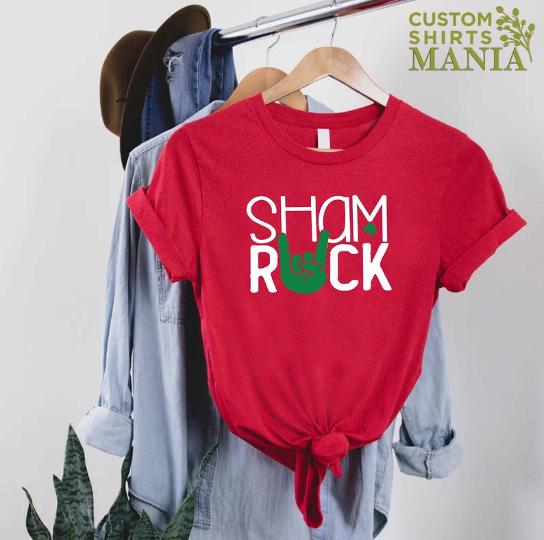 Peut inclure: T-shirt rouge avec du texte blanc qui dit "Shamrock" et un symbole de main rock and roll vert.