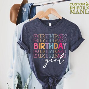 May include: A dark blue t-shirt with a rainbow stacked "Birthday" graphic and the word "girl" in white script.