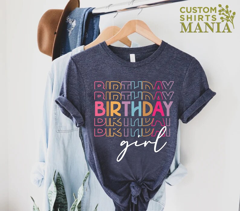 May include: A dark blue t-shirt with a rainbow stacked "Birthday" graphic and the word "girl" in white script.