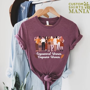 May include: A maroon t-shirt featuring a graphic of a group of diverse women standing together. The text "Empowered Women Empower Women" is printed below the graphic.