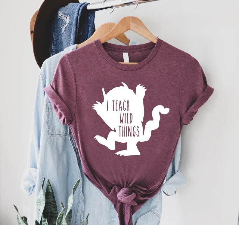 May include: A maroon t-shirt with a white silhouette of a monster and the text "I teach wild things".