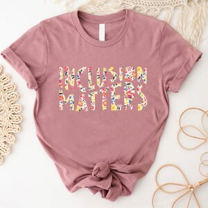 Puede incluir: Una camiseta de color malva con mangas cortas y un dise&ntilde;o de estampado floral que dice "Inclusion Matters".