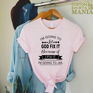May include: Pink t-shirt with black text that reads "I'm going to let... God fix it because if I fix it I'm going to jail."