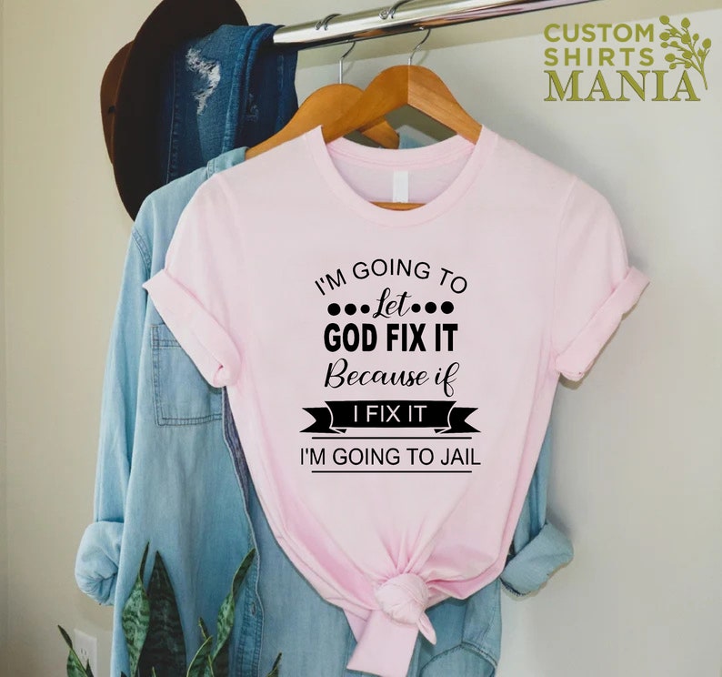 May include: Pink t-shirt with black text that reads "I'm going to let... God fix it because if I fix it I'm going to jail."