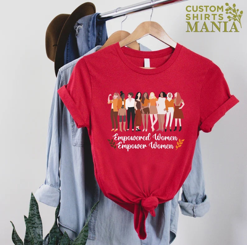 May include: Red t-shirt featuring a graphic of a group of women standing together. The text "Empowered Women Empower Women" is printed below the graphic.