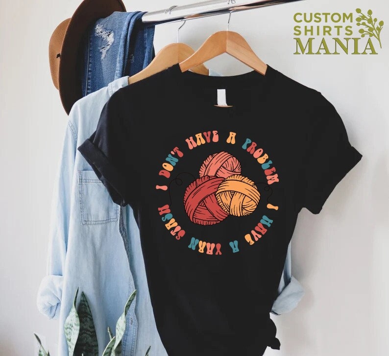 May include: Black t-shirt with a colorful graphic that says "I don't have a problem I have a yarn stash". The graphic features three balls of yarn in red, orange, and yellow.