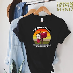 May include: A black t-shirt with a vintage-style graphic of a red mailbox with the text "I'm into fitness. Fit'ness this whole package into your mailbox."