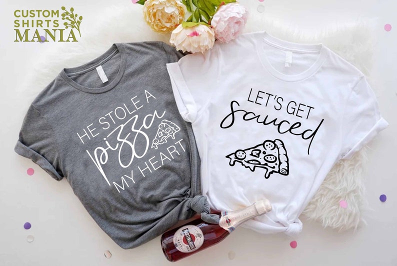Puede incluir: Dos camisetas grises y blancas con un gr&aacute;fico de pizza y el texto "He stole a pizza my heart" y "Let's get sauced".