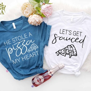 Puede incluir: Dos camisetas con tem&aacute;tica de pizza. Una camiseta es azul turquesa con el texto "Se rob&oacute; una pizza mi coraz&oacute;n" y un peque&ntilde;o gr&aacute;fico de pizza. La otra camiseta es blanca con el texto "Vamos a emborracharnos" y un gr&aacute;fico de pizza m&aacute;s grande.