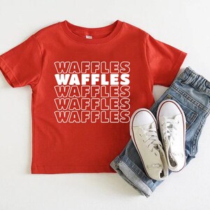 Może przedstawiać: Czerwona koszulka z kr&oacute;tkim rękawem z napisem "Waffles" powt&oacute;rzonym cztery razy białym tekstem.