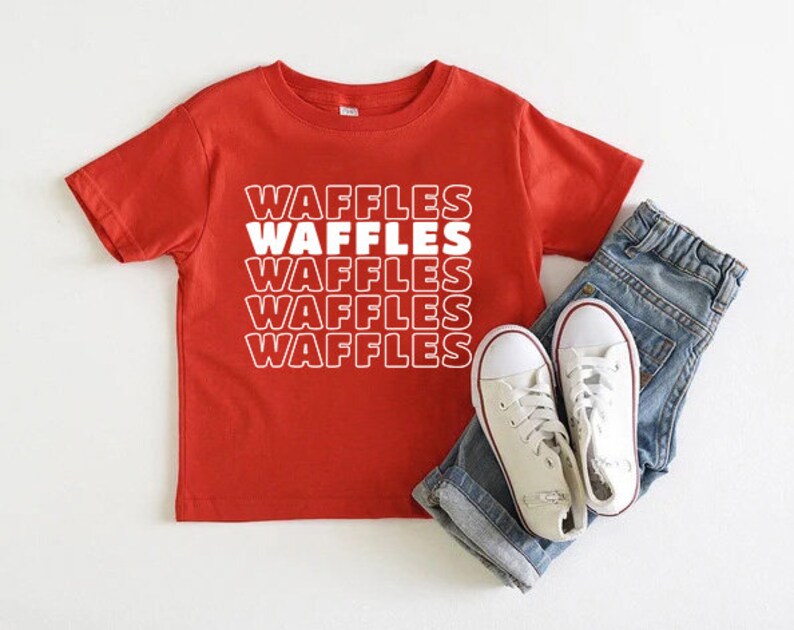 Może przedstawiać: Czerwona koszulka z kr&oacute;tkim rękawem z napisem "Waffles" powt&oacute;rzonym cztery razy białym tekstem.
