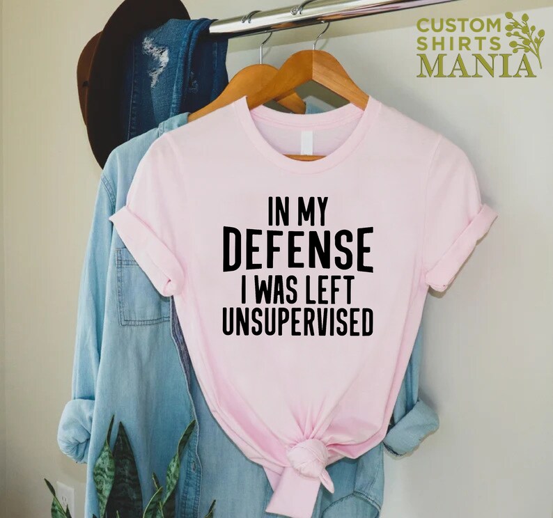 May include: A pink t-shirt with the text "In my defense I was left unsupervised" printed in black.