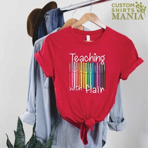 May include: Red t-shirt with the text "Teaching with flair" and a graphic of colorful markers.