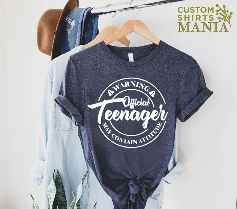 May include: A navy blue t-shirt with a white circle graphic that says "Warning Official Teenager May Contain Attitude".