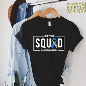 May include: Black t-shirt with a white rectangle that says "Support Squad" with a blue ribbon with a red dot in the center. The text below the rectangle says "Diabetes Awareness".