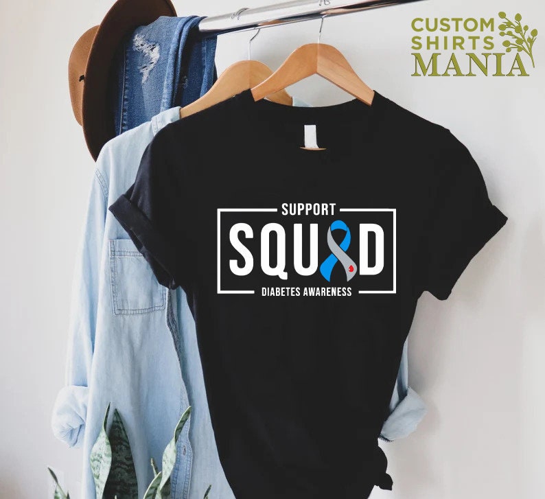 May include: Black t-shirt with a white rectangle that says "Support Squad" with a blue ribbon with a red dot in the center. The text below the rectangle says "Diabetes Awareness".
