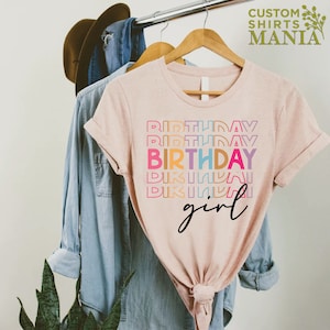 May include: A pink t-shirt with the text "Birthday girl" in rainbow colours. The text is stacked and the word "Birthday" is repeated multiple times.